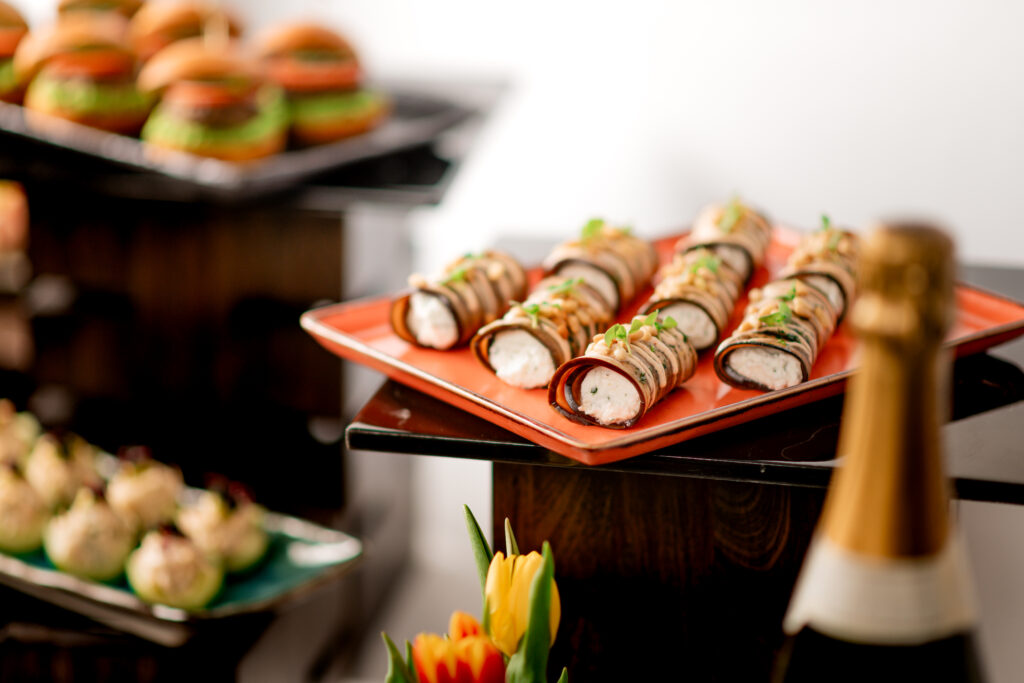 A selection of canapés neatly laid out. In the foreground the top of a champagne bottle is visable.